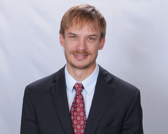 A man in a suit and tie posing for a portrait with a neutral background.