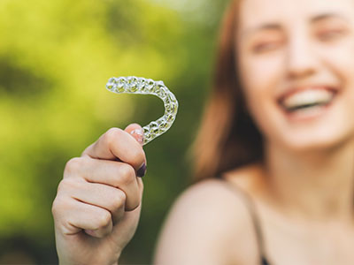 A smiling woman holding up a clear dental retainer with her hand.