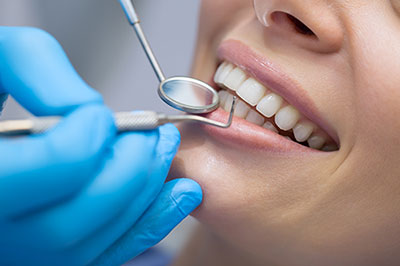 The image shows a person receiving dental care, with a dental professional performing a procedure on their teeth while wearing protective gloves and using specialized equipment.