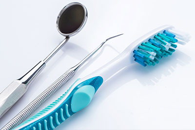 The image shows dental tools including a toothbrush, dental pick, and dental mirror next to a pair of scissors with blue handles on a white background.