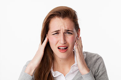 The image shows a woman with her hand on her head, appearing to be experiencing discomfort or pain.