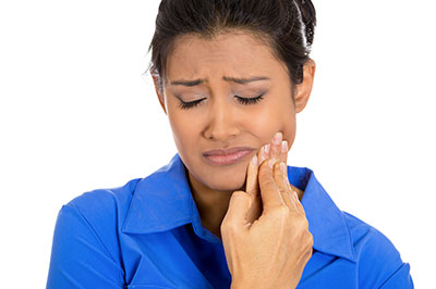 The image shows a woman with her eyes closed, holding her face and appearing to be in pain or discomfort, while looking at something off-frame with an expression of concern.