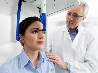 The image shows a woman seated in a dental chair with a blue headgear on her head, receiving treatment from a dentist who is standing next to her.