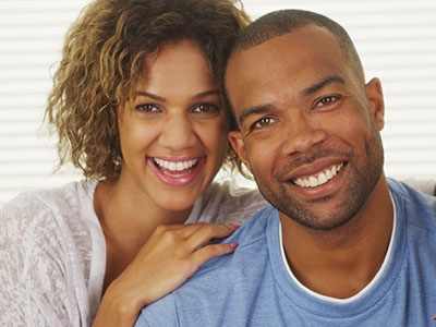 The image shows a man and a woman smiling at the camera  the man has a beard, both are wearing casual clothing, and they appear to be posing for a photograph.