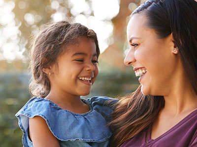 The image shows a woman and a young child smiling at the camera, with the woman holding the child.