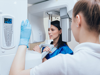 A woman in a blue coat is standing next to a large white 3D scanner machine, with another person in a white lab coat observing the device.