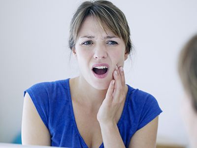 A woman with her mouth open and hand on her chin, looking into a mirror, expressing surprise or concern.