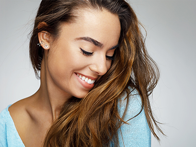 The image features a woman with long hair smiling gently at the camera against a plain background.