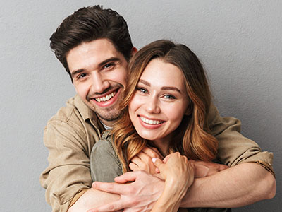 A young couple embracing and smiling at each other against a neutral background.