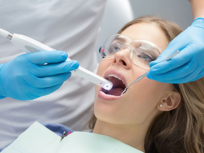 A woman receiving dental treatment with a dentist using a digital device to scan her teeth.