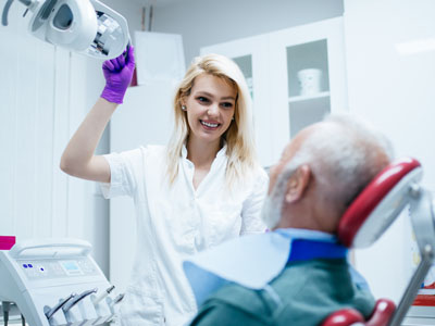 A dental professional assisting an elderly patient with dental equipment.