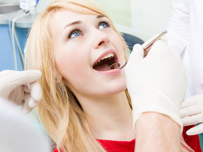 A woman receiving dental care, sitting in a dentist s chair with her mouth open, while a professional attendant works on her teeth with tools visible.