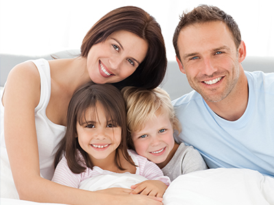 A family of four with two adults and two children posing together on a bed.