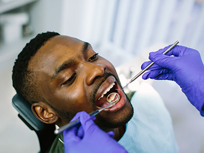 The image shows a person receiving dental care, with a dentist performing a procedure while wearing gloves and using dental instruments.